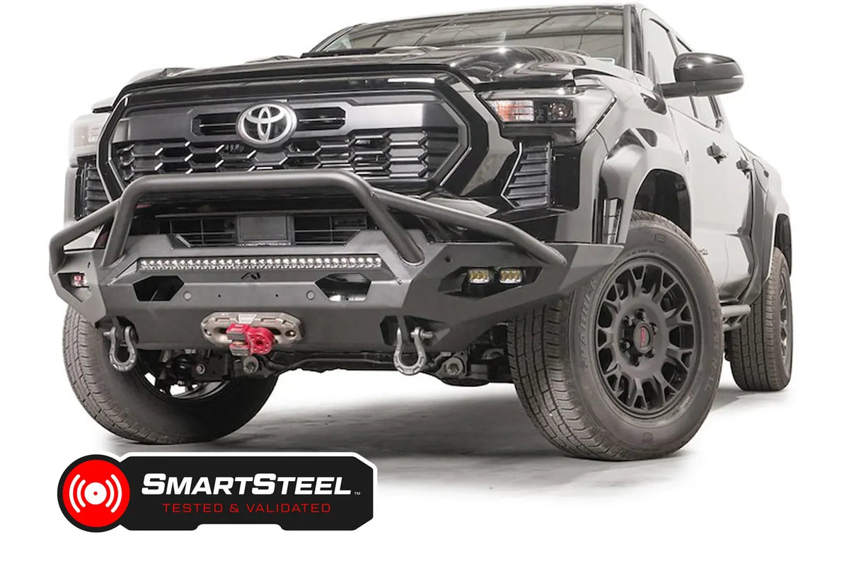 Fab Fours Matrix front bumper with pre-runner guard on a black Toyota Tacoma, front three-quarter view, showing the pre-runner hoop, LED light bar, and winch with red hook