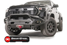 Fab Fours Matrix front bumper with pre-runner guard on a black Toyota Tacoma, front three-quarter view, showing the pre-runner hoop, LED light bar, and winch with red hook