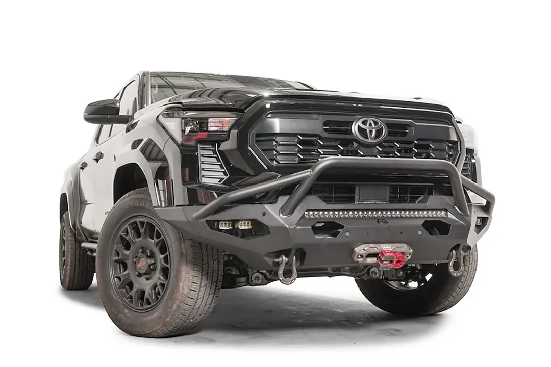 Fab Fours Matrix front bumper with pre-runner guard on a black Toyota Tacoma, front three-quarter view, showing the pre-runner hoop, LED light bar, and winch with red hook