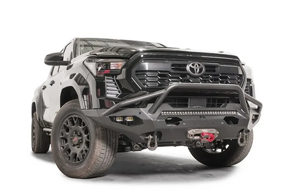 Fab Fours Matrix front bumper with pre-runner guard on a black Toyota Tacoma, front three-quarter view, showing the pre-runner hoop, LED light bar, and winch with red hook