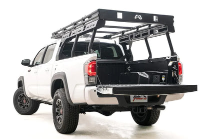 Fab Fours Overland Rack on a white Toyota Tacoma TRD Pro, rear driver-side view with the tailgate down, showing the black platform, tubular uprights and modular side panels over the bed