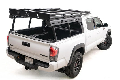 Fab Fours Overland Rack on a white Toyota Tacoma TRD Pro, rear passenger-side view, showing the platform with crossbars, slotted side panels and tubular uprights above the open bed