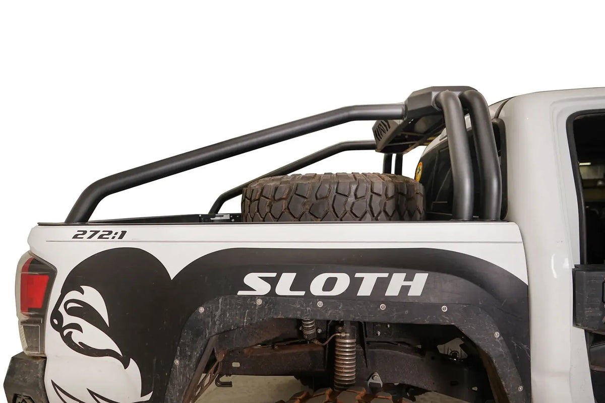 Close-up of Fab Fours sport rack tubes over the bed of a white Toyota Tacoma, passenger side, with spare tire in the bed
