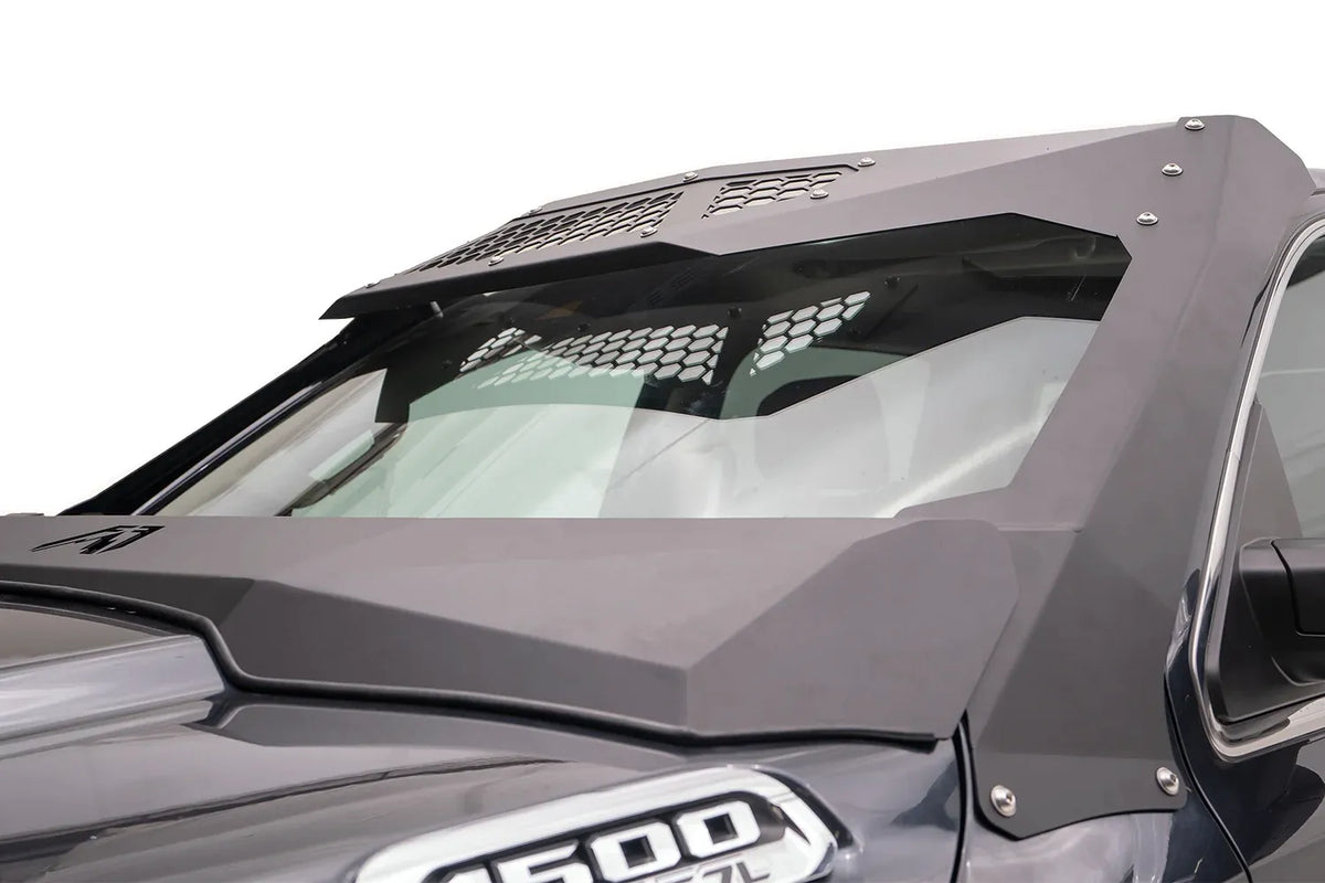 Fab Fours ViCowl on a gray Ram 1500, driver-side close-up, showing the matte black steel cowl and roof visor with honeycomb vent panels framing the windshield