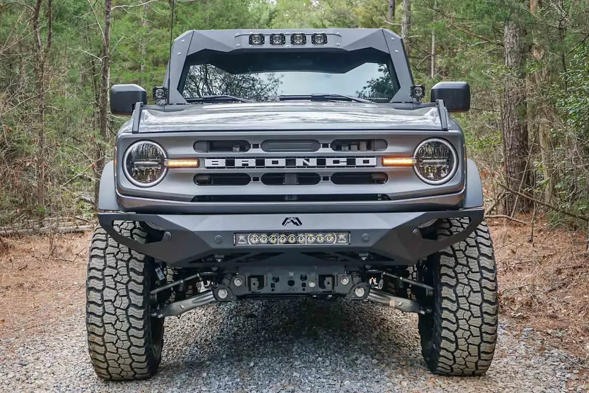 Fab Fours ViCowl on a lifted gray Ford Bronco on a gravel trail, front view, with four cube lights in the visor and a Fab Fours front bumper with LED light bar