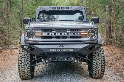 Fab Fours ViCowl on a lifted gray Ford Bronco on a gravel trail, front view, with four cube lights in the visor and a Fab Fours front bumper with LED light bar