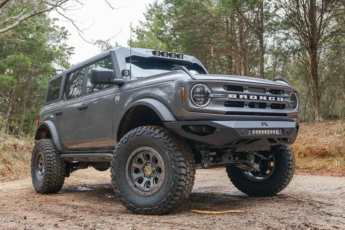 Fab Fours ViCowl on a lifted gray four-door Ford Bronco outdoors, front passenger-side view, with the visor light insert and a matching Fab Fours front bumper with LED light bar