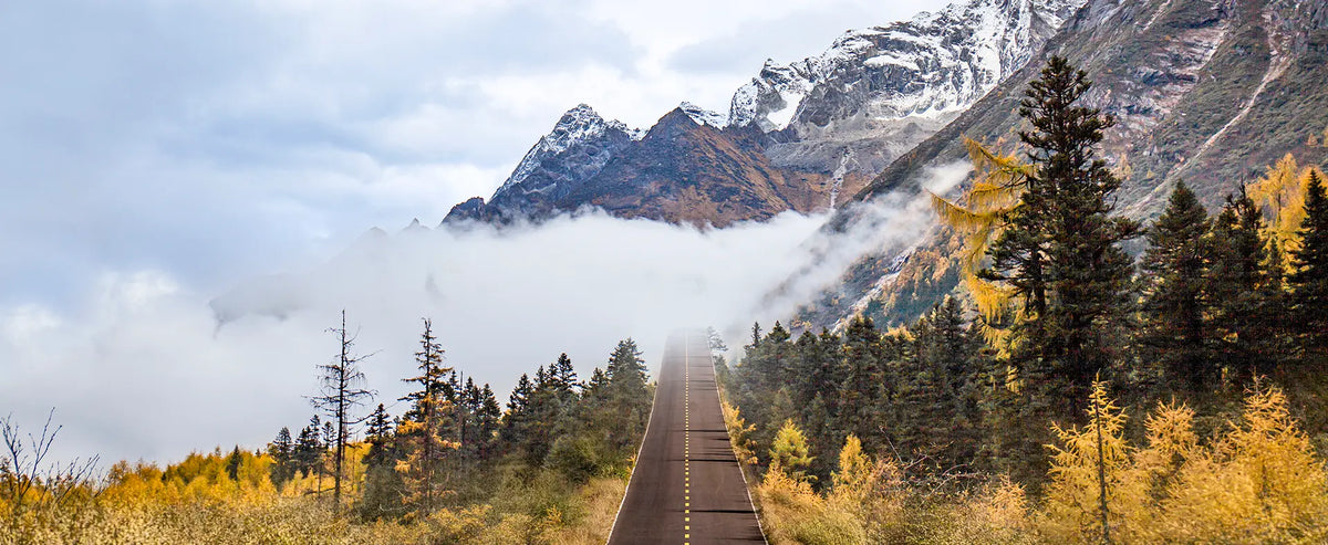 Straight mountain road leading into fog beneath snow-capped peaks