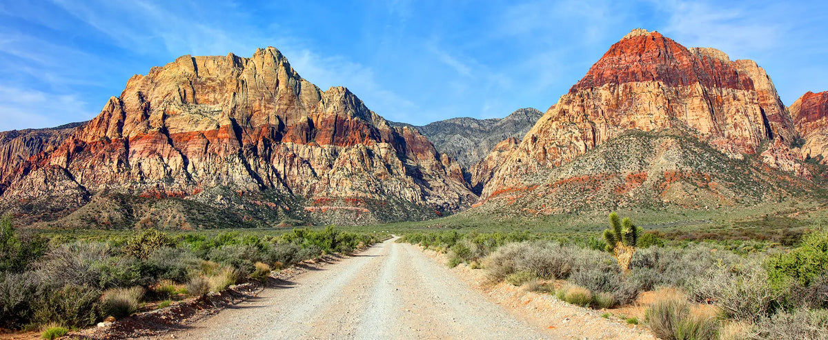 Dirt road leading toward red rock canyon mountains under a blue sky